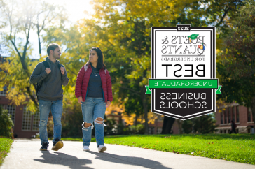 Two students walk along a path in fall alongside the Poets&Quants 2023 best business schools badge